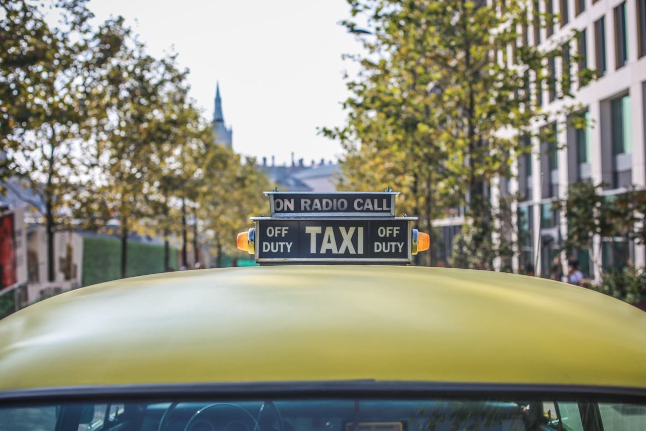 A yellow taxi with a prominent sign parked in a sunlit urban street with modern buildings.