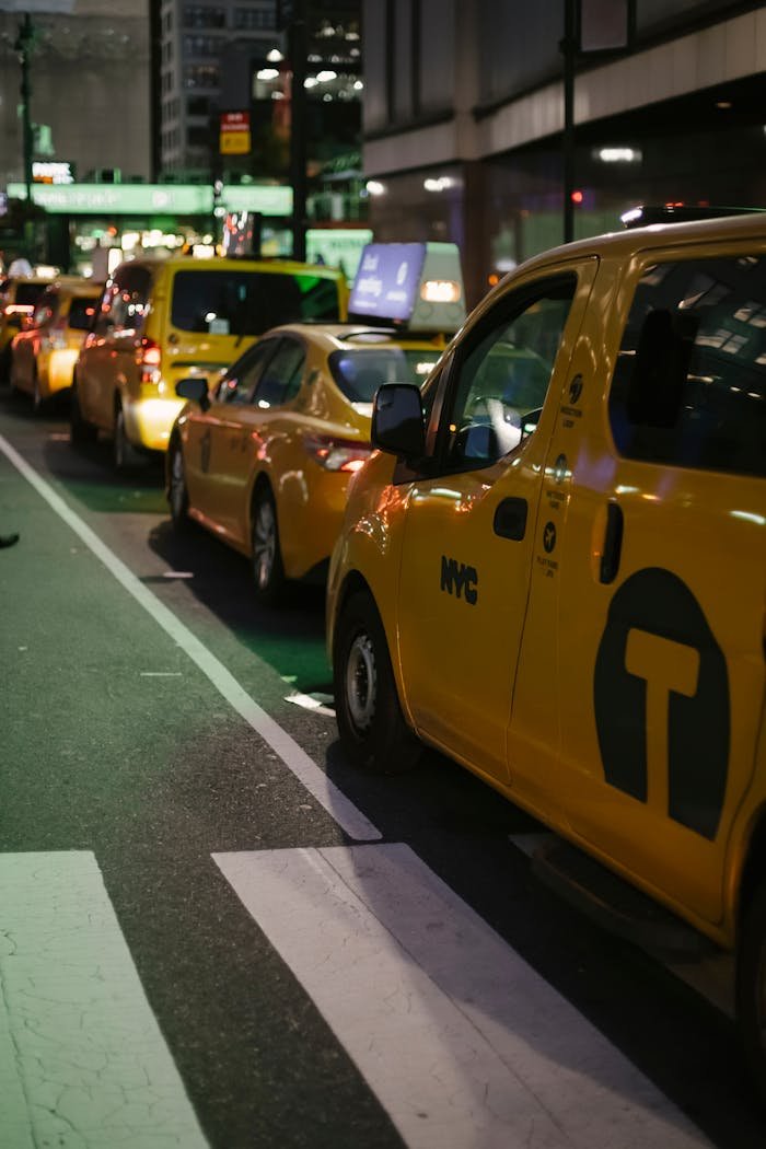 Yellow taxis line a bustling street in New York City at night, illuminating the urban landscape.