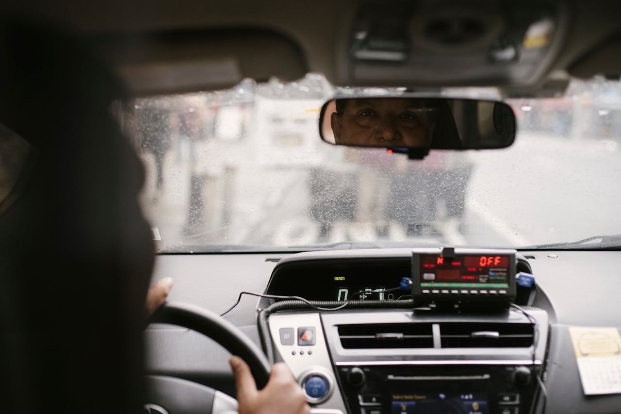 Back view of man reflecting in mirror while driving along street in city on urban background in soft daylight
